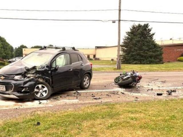 Black SUV with severe front-end damage after a collision on a road, debris scattered across the street, and a toppled motorcycle nearby.