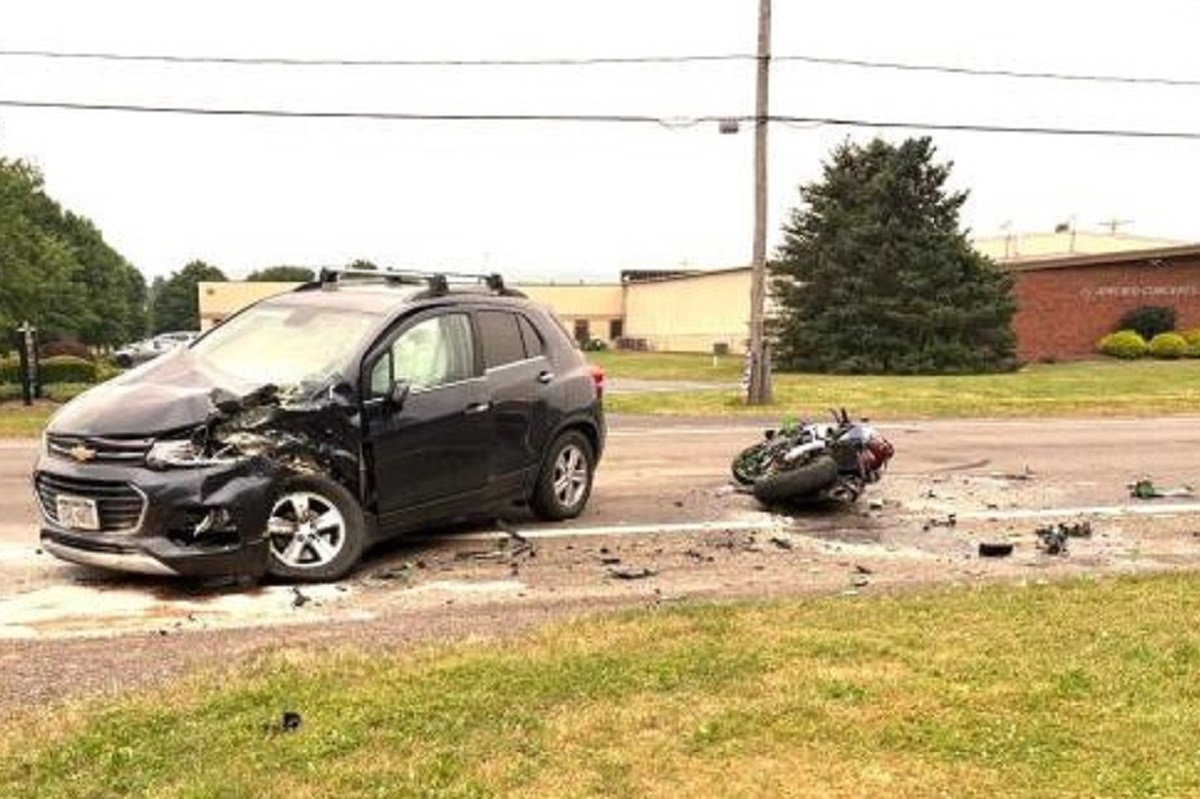 Black SUV with severe front-end damage after a collision on a road, debris scattered across the street, and a toppled motorcycle nearby.